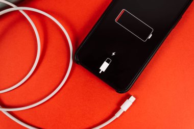 Kırmızı arkaplanda akıllı telefon ve ekranda düşük pil simgesi.