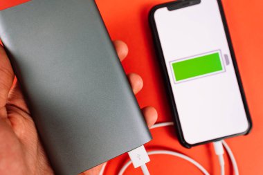 Kırmızı arkaplanda akıllı telefon ve ekranda düşük pil simgesi.