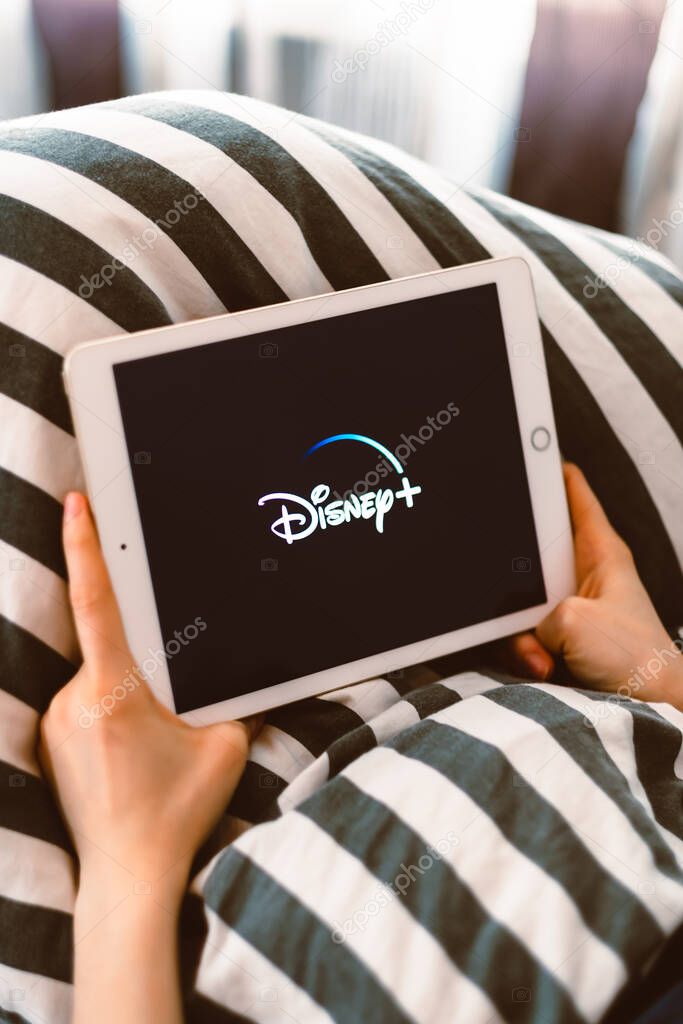 Girl holding a tablet with Disney plus logo on the screen. High quality photo.