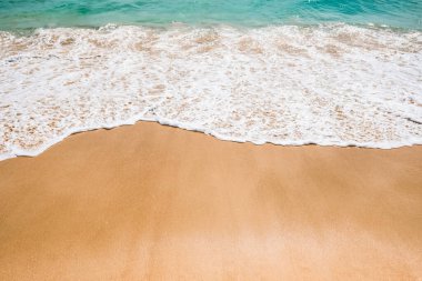 Yumuşak mavi dalgalar, kumlu sahil arka planında okyanus köpüğü..