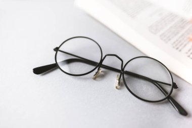 Okuma gözlükleri ve gri arkaplan üzerine bir kitap..