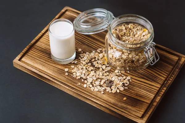 Granola em um frasco de vidro com um copo de leite, ficar em uma placa de madeira . — Fotografia de Stock