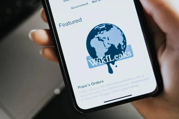 Mãos segurando iPhone X com Wikileaks site logotipo home page na tela . — Fotografia de Stock