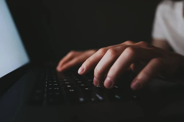 Mujer está escribiendo en un teclado portátil mientras está acostado en un sofá en casa en la oscuridad . — Foto de Stock