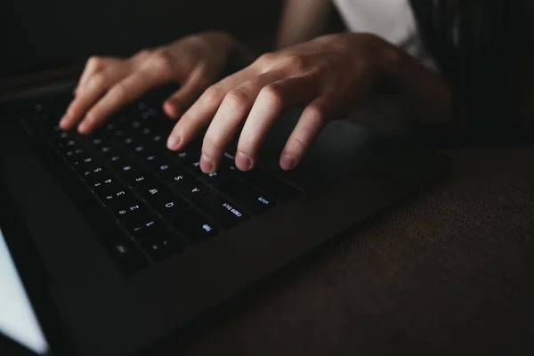 Mujer está escribiendo en un teclado portátil mientras está acostado en un sofá en casa en la oscuridad . — Foto de Stock