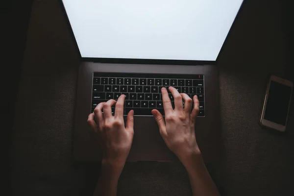 Mujer está escribiendo en un teclado portátil mientras está acostado en un sofá en casa en la oscuridad . — Foto de Stock
