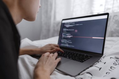 Genç bayan programcı yataktaki bir bilgisayar dizüstü bilgisayarına program kodu yazar. . 