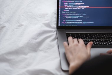 Kadın programcı yataktaki bir bilgisayar dizüstü bilgisayarına program kodu yazar. . 