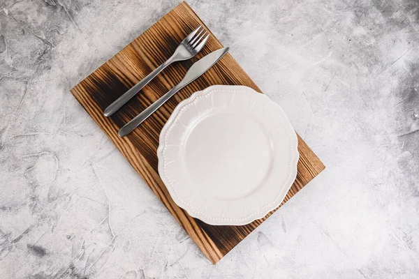 Piatto bianco vuoto su una tavola di legno con posate . — Foto Stock
