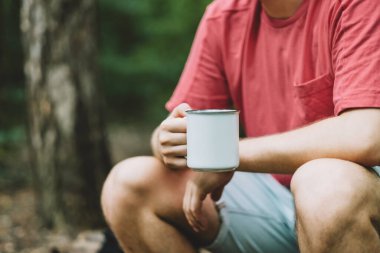 Ormanda mola verilirken beyaz bardaktan su içen bir adam. Yürüyüş, aktif yaşam tarzı. Yüksek kalite fotoğraf