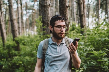 Ormanda akıllı telefon kullanan genç bir adam. Turizm, aktif yaşam tarzı