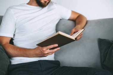 Genç beyaz bir adam kanepede dinleniyor ve kitap okuyor. Ev tatili. Yüksek kalite fotoğraf