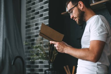 Genç beyaz sakallı adam mutfakta kitap okuyor. Ev tatili. Yüksek kalite fotoğraf