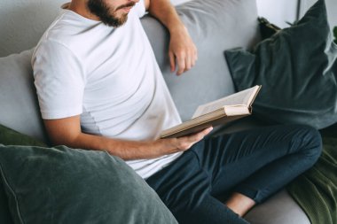 Genç beyaz bir adam kanepede dinleniyor ve kitap okuyor. Ev tatili. Yüksek kalite fotoğraf