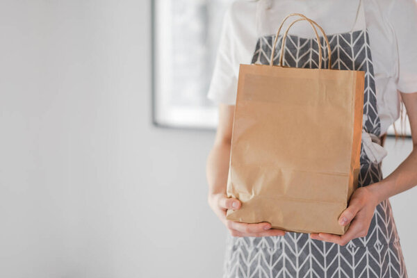 Woman holds craft eco shopping bag in hands, take away. Delivery food, mock up. High quality photo