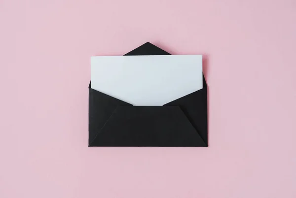 Black envelope with white blank paper in isolated on a pastel pink background. Mock up. High quality photo
