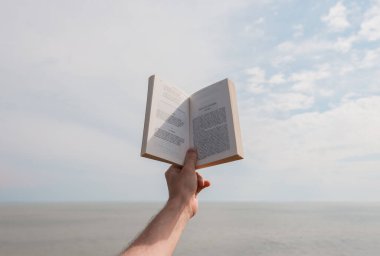 Elinde açık bir kitap, bulutlu deniz ve mavi gökyüzü. Açık hava konsepti okuyorum. Yüksek kalite fotoğraf
