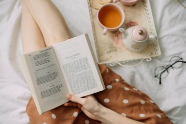 Bir kadın evinde kitap okuyor ve çay içiyor, rahatlık ve rahatlık içinde evde dinleniyor. Yüksek kalite fotoğraf