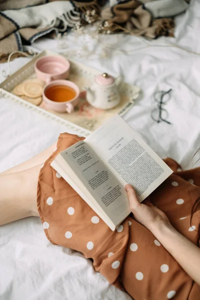 A woman reads a book at home in bed and drinks tea, home leisure in coziness and comfort. High quality photo