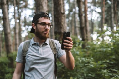 Genç bir adam ormanda akıllı telefon kullanarak video aracılığıyla konuşuyor. Turizm, aktif yaşam tarzı. Yüksek kalite fotoğraf