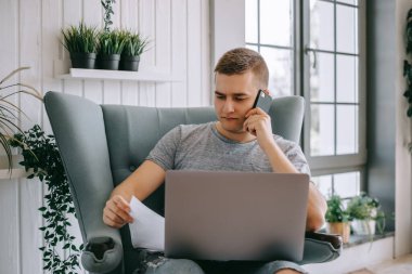 Elinde kağıt belgeler olan odaklanmış beyaz bir adam elinde dizüstü bilgisayarlı bir sandalyede oturuyor mali danışmanı ya da banka çağrı merkezini arıyor, sorun çözmede sorun yaşıyor. Yatırım danışmanlığı.