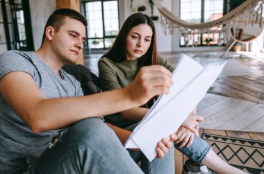 Genç bir çift, oturma odasındaki banka hesaplarına bakarak finansman sağlıyor. Kadın ve erkek birlikte belgelere bakar. Bütçe harcamaları planlanıyor. Yüksek kalite fotoğraf