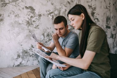 A young couple manages finances by looking through their bank accounts in the living room by the bed. Woman and man look at documents together. Planning budget expenses. High quality photo clipart
