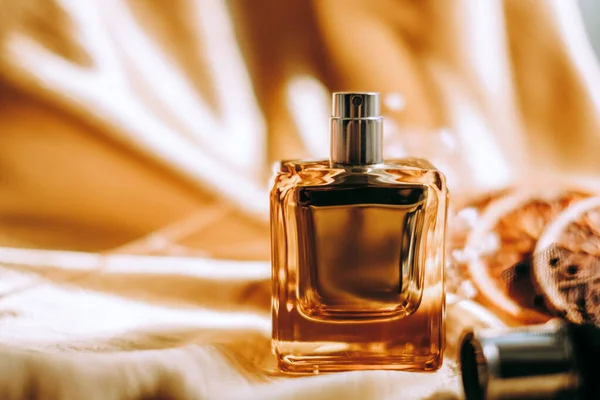 Perfume bottle on golden satin fabric with dried white flowers and orange slices, warm light. High quality photo