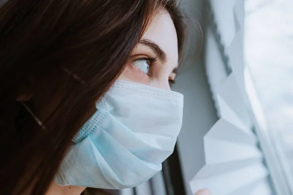 Tıbbi Koruyucu Maskeli Beyaz Bir Kadın Pencereden Dışarı Bakıyor Coronovirus — Stok fotoğraf
