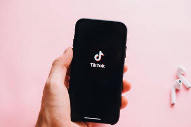 Pembe arka planda TikTok uygulaması logosu olan el ele tutuşan iPhone. Yüksek kalite fotoğraf