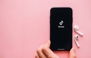 Pembe arka planda TikTok uygulaması logosu olan el ele tutuşan iPhone. Yüksek kalite fotoğraf