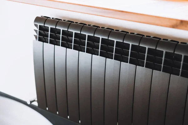 Black aluminum alloy metal heating radiator for home. Black heating battery on the white wall, close-up. High quality photo