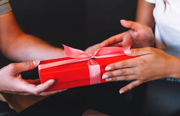 Close up of young man giving his girlfriend red gift box with pink ribbon. Woman receiving unexpected present. Celebrating concept. High quality photo