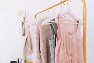 Beyaz duvarın yanında pastel renkli moda kıyafetleri olan altın zemin dolabı. Alışveriş konsepti. Yüksek kalite fotoğraf