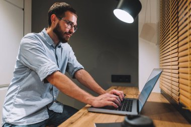 Beyaz sakallı genç adam evde çalışıyor, serbest çalışıyor, dizüstü bilgisayar kullanıyor..