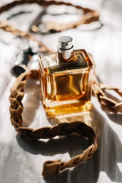 Złota Butelka Perfum Białym Tle Tkaniny Brązowym Plecionym Skórzanym Paskiem — Zdjęcie stockowe