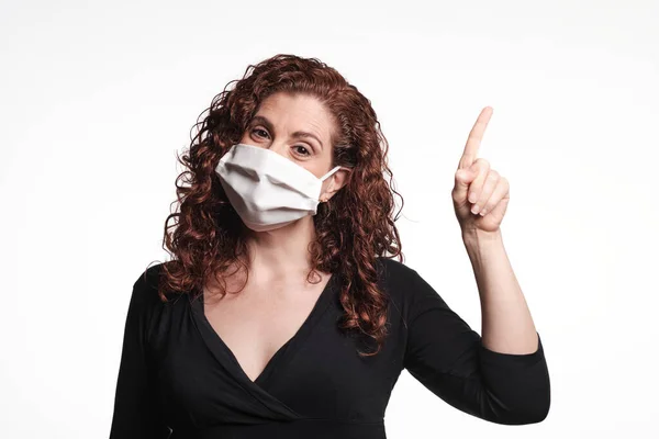 Koronavirüs için koruyucu maske takan ve parmağıyla işaret eden kızıl saçlı kadın.