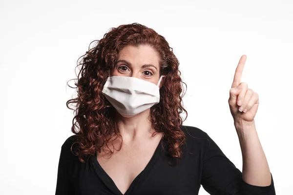 Koronavirüs için koruyucu maske takan ve parmağıyla işaret eden kızıl saçlı kadın.