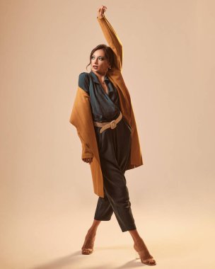 Sarı arka planda yeşil bir elbise ve sarı bir ceket giyen zayıf bir kadının moda portresi.