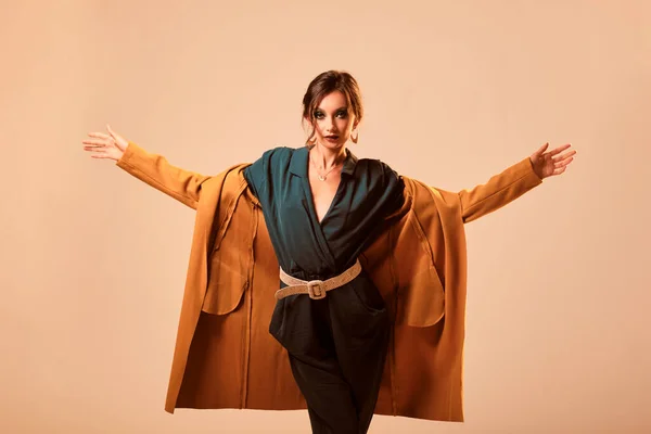 Fashion portrait of a skinny woman wearing a green dress and a yellow coat on a yellow background