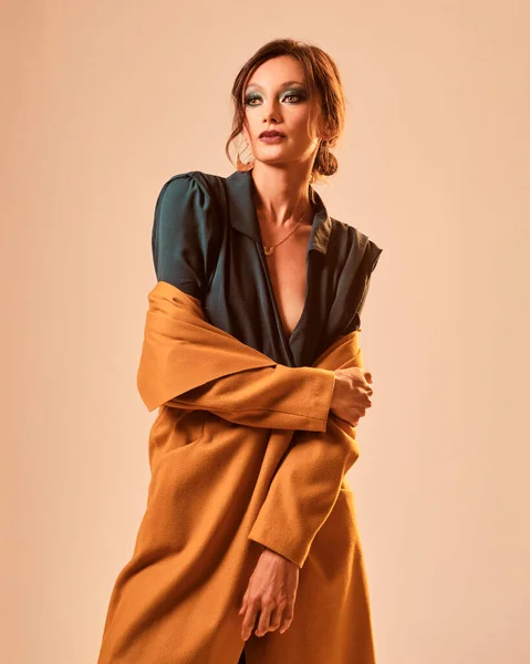 Fashion portrait of a skinny woman wearing a green dress and a yellow coat on a yellow background