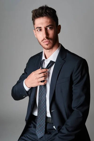 Koyu mavi bir takım elbise ve kırmızı ve açık mavi noktalı koyu mavi bir kravat giyen genç adam portresi. Kravat düğümünü çözüyor..