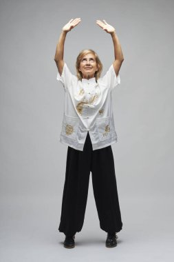 Olgun sarışın kadın beyaz arka planda Chi kung ve Tai Chi çalışıyor. Geleneksel beyaz Çin Tai Chi ceketi, siyah pantolon ve ying yang sembollü siyah ayakkabılar giyiyor.