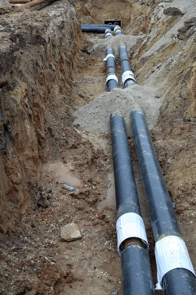 Черные стальные трубы водопровода в земляной канаве
