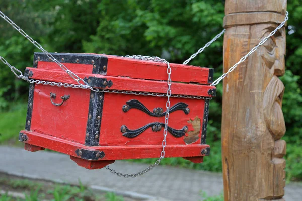 Red decorative chest of natural wood hanging on chains in the backyard