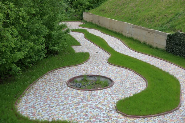 A winding path for walks from stone tiles among trees and a green lawn