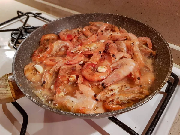 Giant orange shrimps with heads fried in oil in a frying pan on a gas stove