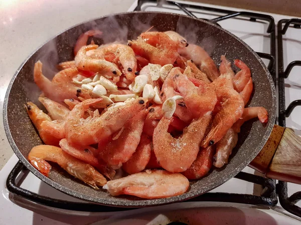 Giant orange shrimps with heads fried in oil in a frying pan on a gas stove