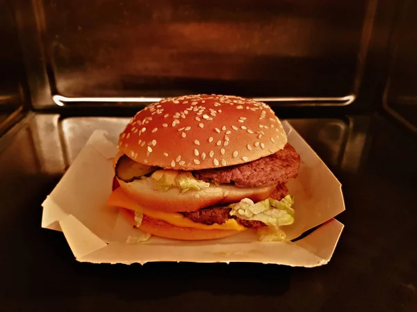 Großer saftiger Cheeseburger in einer stählernen Mikrowelle — Stockfoto