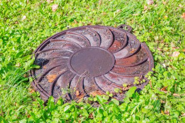 Yeşillik çimenlerin arasında eski, yuvarlak bir rögar.